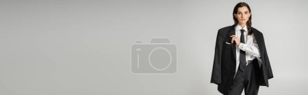 Téléchargez les photos : Young brunette woman in black oversize suit and white shirt looking at camera isolated on grey, banner - en image libre de droit