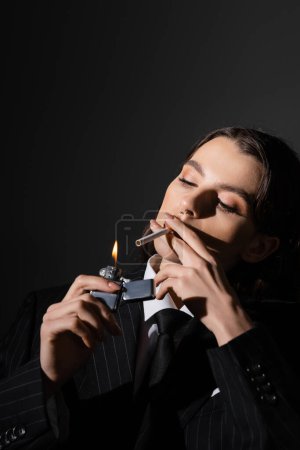Foto de Young and elegant woman in formal wear lighting cigarette isolated on black - Imagen libre de derechos