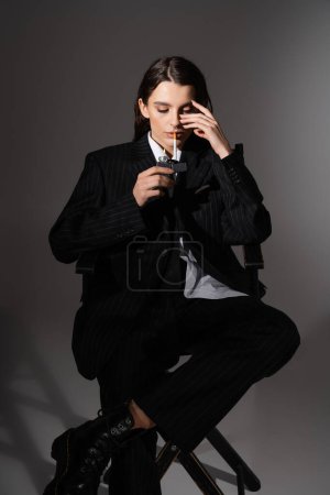 Photo for Fashionable woman in black pantsuit lighting cigarette while sitting on dark grey - Royalty Free Image