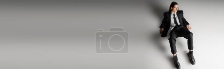 Foto de High angle view of stylish woman in formal wear and laced-up boots sitting on grey background, banner - Imagen libre de derechos
