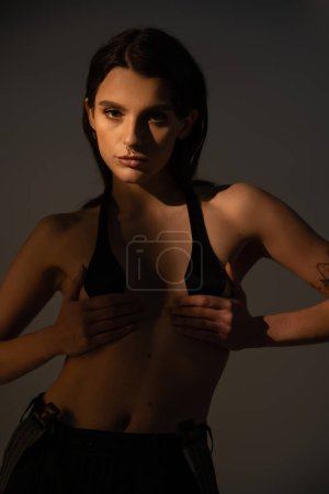 sexy shirtless woman in black breast tape looking at camera on grey background with lighting