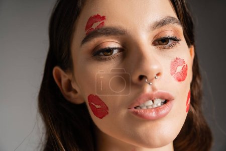 close up portrait of sensual woman with makeup and red kiss prints on face isolated on grey