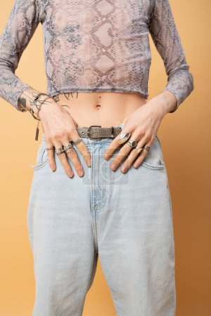 Cropped view of tattooed queer person with accessories isolated on yellow 