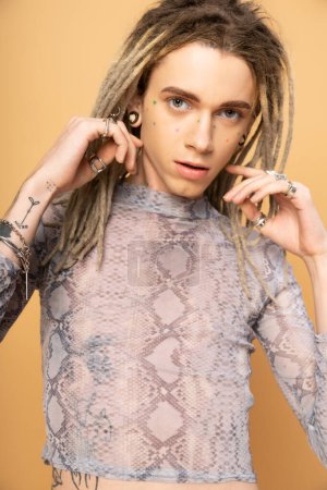 Portrait of tattooed queer person with dreadlocks looking at camera isolated on yellow 