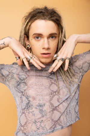 Portrait of tattooed queer person with rings on fingers looking at camera isolated on yellow 