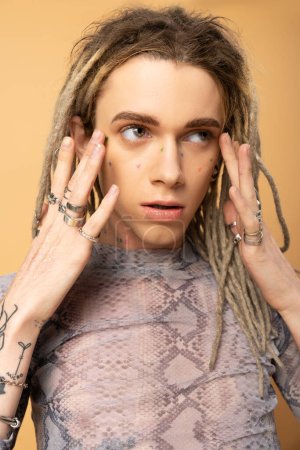 Portrait of queer person with dreadlocks touching face on yellow background 