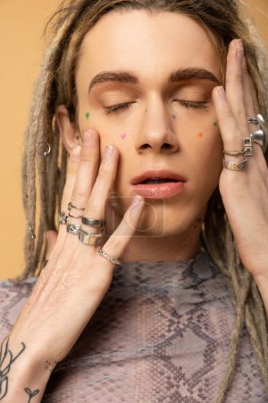 Portrait of young queer person with dreadlocks touching face isolated on yellow 