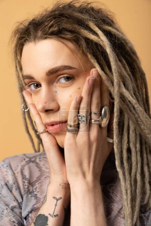 Portrait of tattooed nonbinary person touching face isolated on yellow 