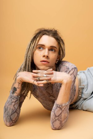 Portrait of tattooed queer person with dreadlocks posing on yellow background 