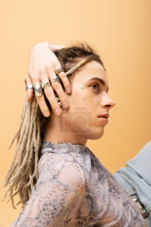 Stylish nonbinary person with silver rings on fingers isolated on yellow 