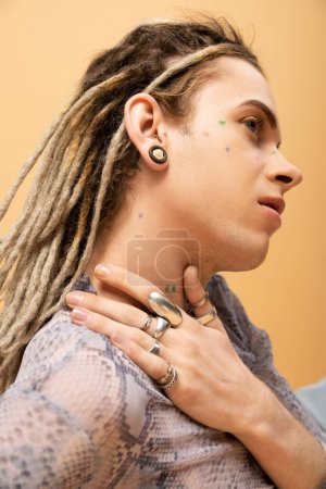Tattooed nonbinary person with dreadlocks and rings posing isolated on yellow 