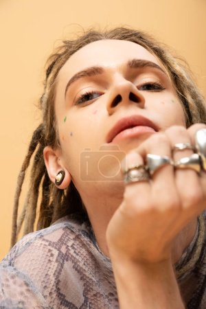 Low angle view of tattooed nonbinary person looking at camera isolated on yellow 