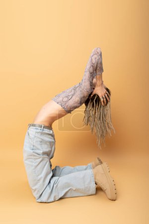 flexible queer person with dreadlocks posing on yellow background 
