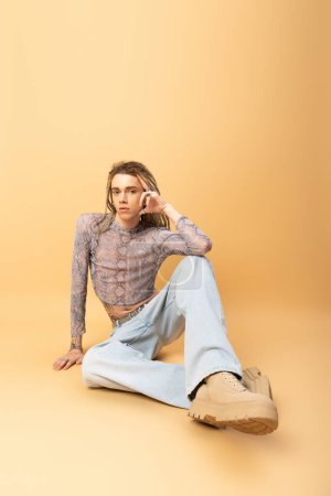 Full length of nonbinary person looking at camera while sitting on yellow background 