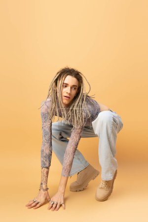 Stylish queer person in jeans and boots posing on yellow background 