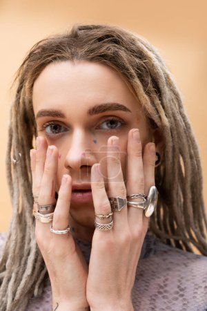 Portrait of queer person with rings on fingers looking at camera isolated on yellow 