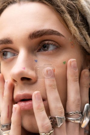 Close up view of young queer person with silver rings on fingers looking away 