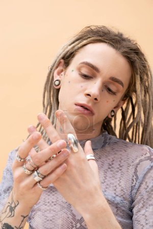 Portrait of nonbinary person touching silver rings on fingers isolated on yellow 