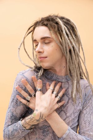 Pleased queer person with dreadlocks touching chest isolated on yellow 