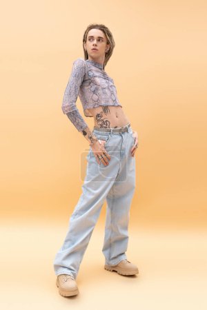 Photo for Full length of trendy nonbinary person posing in crop top and jeans on yellow background - Royalty Free Image