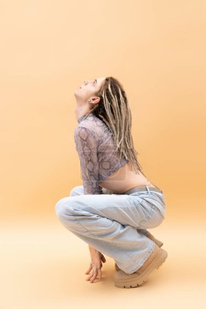 Photo for Side view of queer person in crop top with snakeskin print and jeans looking up on yellow background - Royalty Free Image