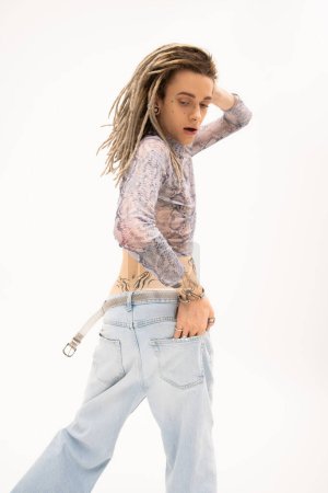 Téléchargez les photos : Tattooed queer person in crop top with snakeskin print and jeans posing isolated on white - en image libre de droit