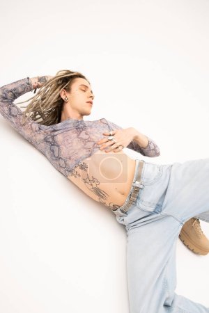 Photo for Young tattooed queer person in jeans and crop top posing on white background - Royalty Free Image