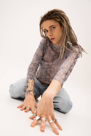 Tattooed queer person with rings on fingers looking at camera on white background