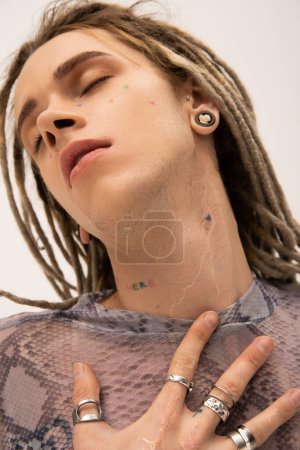 Portrait of young tattooed nonbinary person posing with closed eyes isolated on white 
