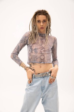 Tattooed nonbinary person in crop top touching jeans isolated on white 