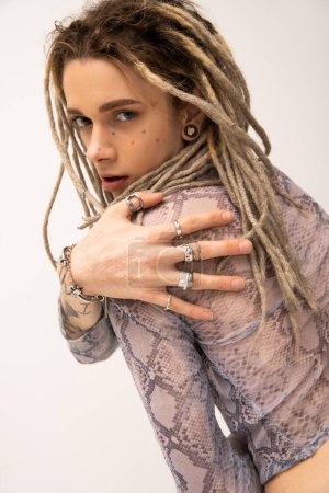 young queer person with dreadlocks and silver finger rings looking at camera isolated on white