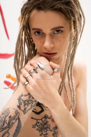 Foto de Stylish queer person with tattoo and silver finger rings looking at camera on white - Imagen libre de derechos