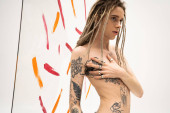 shirtless queer person with dreadlocks touching tattooed torso near multicolored paint strokes on white background magic mug #636817240