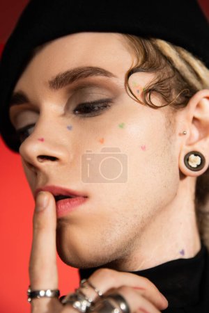 close up portrait of tattooed queer person with makeup touching lips isolated on orange