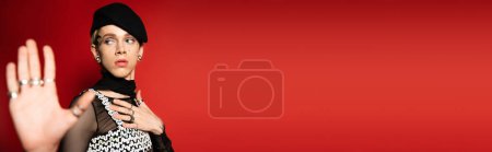 Téléchargez les photos : Elegant nonbinary person in black beret showing stop gesture isolated on red, banner - en image libre de droit