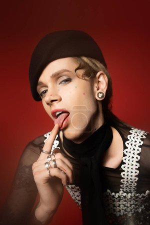 queer person in elegant attire sticking out tongue and looking at camera on red background