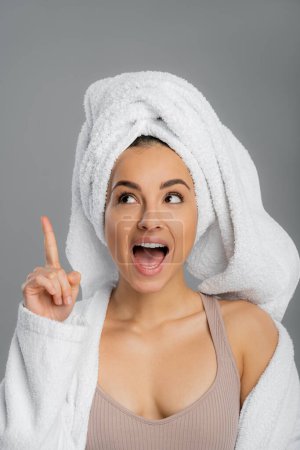 Excited young woman with towel on head pointing with finger isolated on grey 