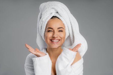 Positive young woman with towel on head looking at camera isolated on grey 