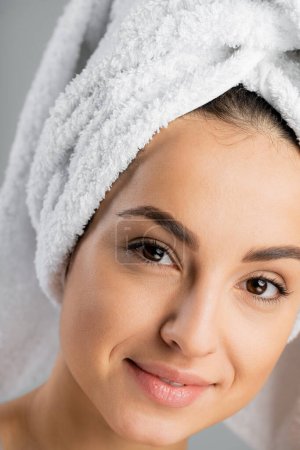 Portrait of young woman with perfect skin and towel on head looking at camera isolated on grey 
