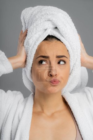 Foto de Thoughtful woman in bathrobe touching towel on head isolated on grey - Imagen libre de derechos