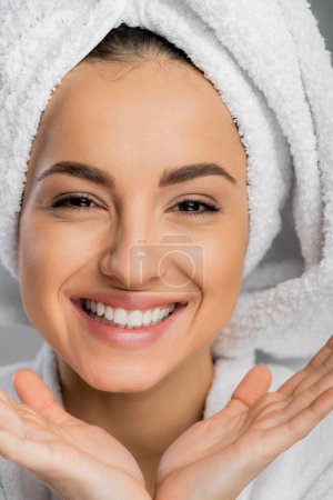 Portrait of positive woman with perfect skin and towel on head isolated on grey 