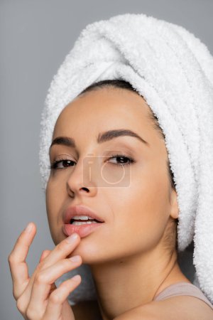 Woman with towel on head touching lip isolated on grey 