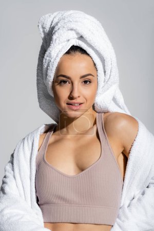 Portrait of woman in bathrobe and towel smiling at camera isolated on grey 