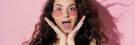 Excited brunette woman with hydrogel eye patches on face on pink background, banner  