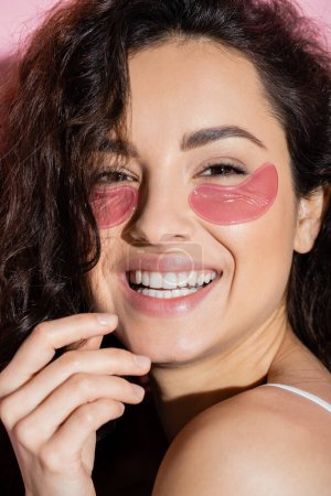 Portrait of curly young woman with eye patches looking at camera on pink background 