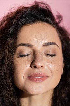 Portrait of smiling freckled woman closed eyes isolated on pink 