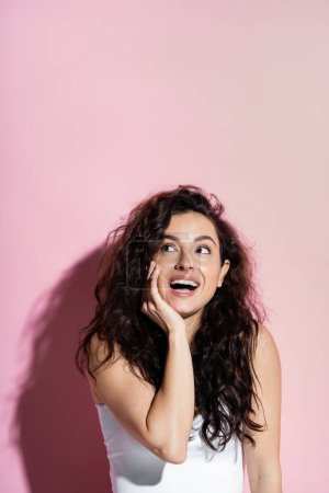 Positive freckled woman in top looking away on pink background 