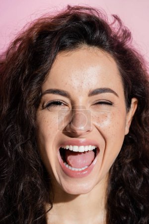 Téléchargez les photos : Portrait of excited and curly freckled woman looking at camera isolated on pink - en image libre de droit