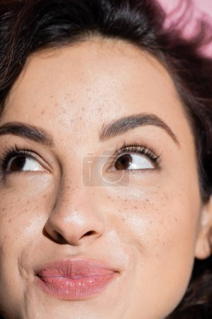Close up view of pleased and freckled woman looking up 
