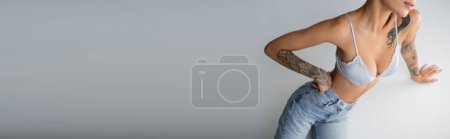 Photo for Cropped view of seductive woman in jeans and bra posing with hand on hip near cube on grey background, banner - Royalty Free Image